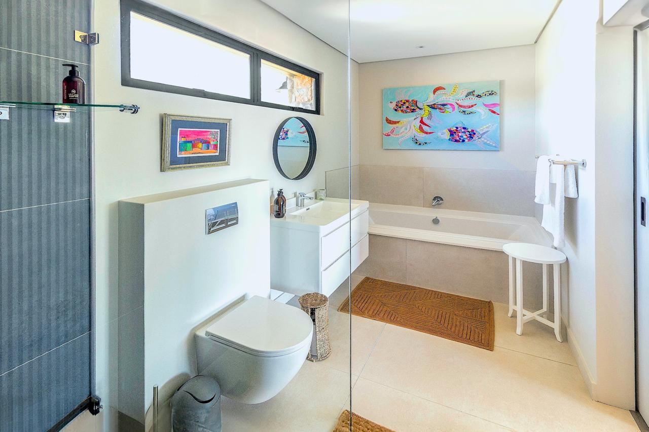 Spacious bathroom with bathtub, vibrant artwork, and glass shower